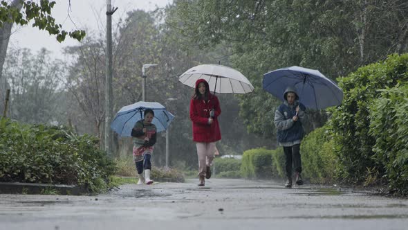 Three kids running happy in the rain and puddles with umbrellas alt