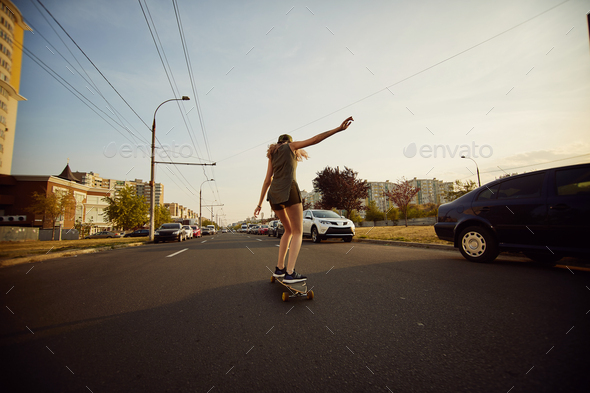 Beautiful young girl with tattoos riding longboard in sunny weather - Stock Photo - Images