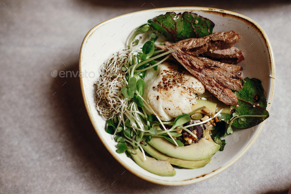 Delicious salad with juicy grill steak, avocado, sprouted greens, leaves, egg pouch, nuts - Stock Photo - Images