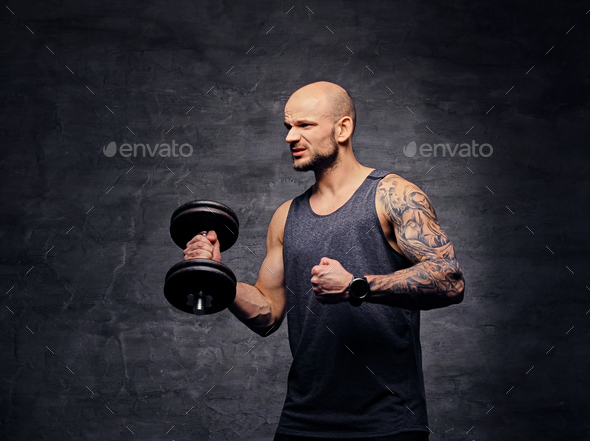 Athletic shaved head tattooed male doing biceps workout with dumbbell.