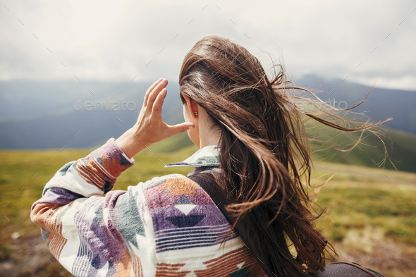 traveler hipster girl with windy hair and backpack, standing on top of sunny mountains - Stock Photo - Images