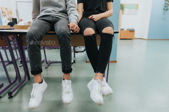Two teenagers are sitting on the table and holding hands - Stock Photo - Images
