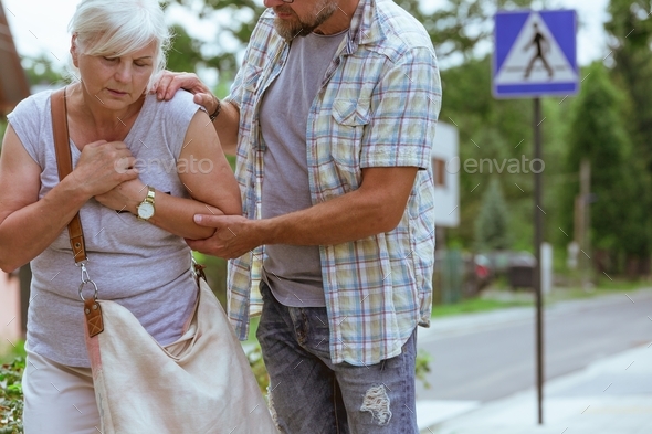 Man is supporting a senior woman feeling unwell on the street - Stock Photo - Images