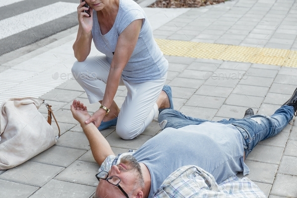 Senior passerby kneels beside the person who fainted on the street and calls an ambulance