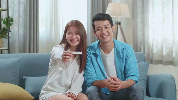 Happy Asian Couple Smiling To Camera After Find Out Positive Pregnancy Test In Living Room At Home alt