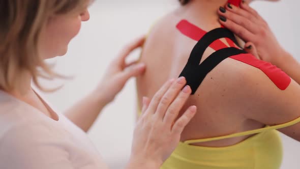 Female doctor helps woman by putting kinesio tape on her shoulder alt