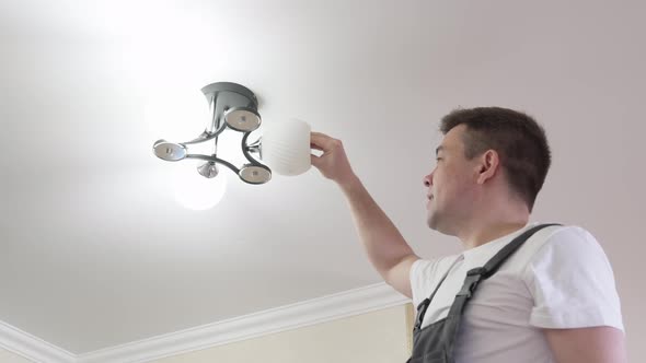 A Male Electrician Changes the Light Bulbs in the Ceiling Light alt