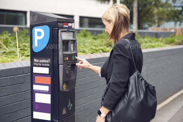 Mature Businesswoman Paying For Car Parking At Machine On City Street