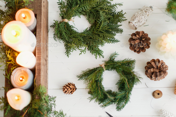 Rustic christmas wreath with candles, pine cones, ornaments on white wooden table, flat lay - Stock Photo - Images