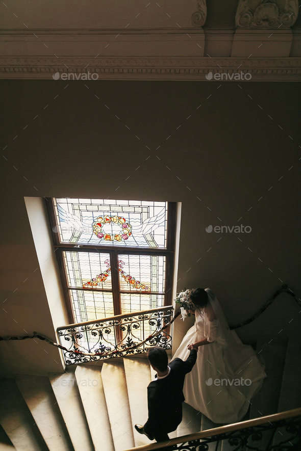 stylish groom with gorgeous bride in amazing dress walking down stairs - Stock Photo - Images