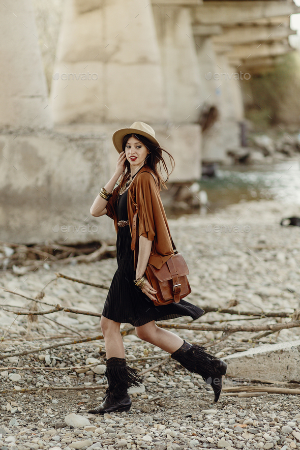 beautiful stylish hipster woman walking with hat, leather bag, fringe poncho and boots - Stock Photo - Images