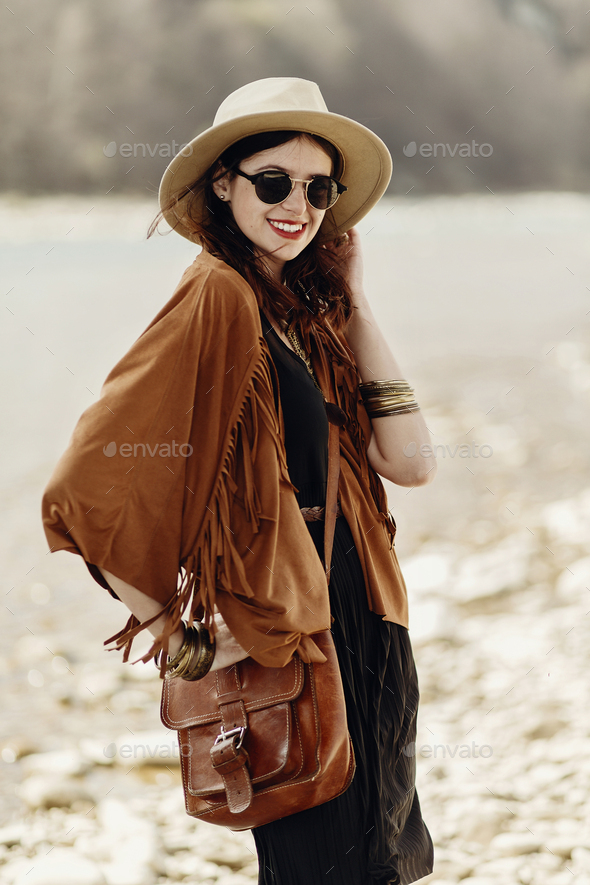 stylish hipster woman posing in hat with windy hair, in fringe poncho and accessory - Stock Photo - Images