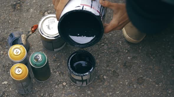 Artist Stir a Black Paint Into a Can and Pouring It to Another Can