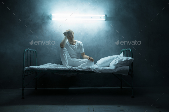 Psycho man sitting in bed, dark room on background - Stock Photo - Images