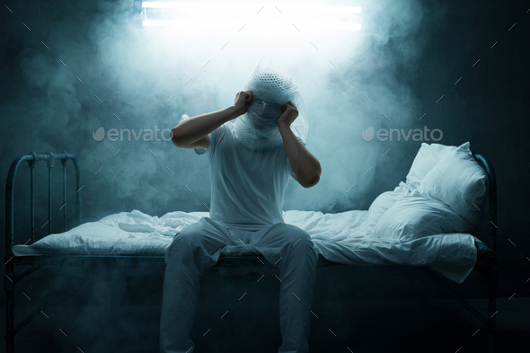 Psycho man sitting in bed, dark room on background