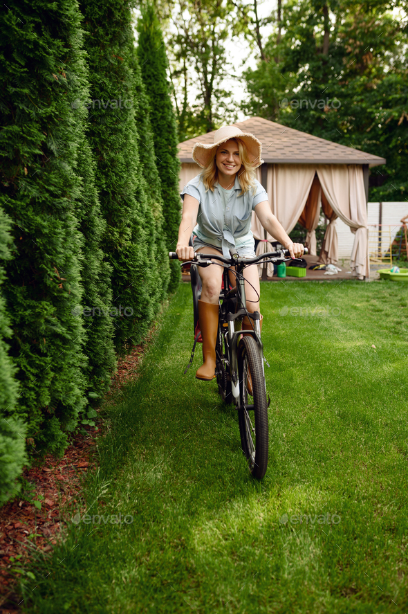 Photo of cheerful woman dressed casually, rides bicycle, looks aside, has  happy expression, wears shades, poses near river, green lawn and trees,  some Stock Photo - Alamy