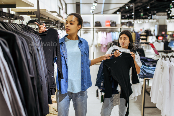 Girls take clothes on hangers in clothing store Stock Photo by