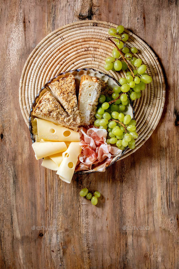 Appetizers antipasti with white sicilian focaccia. Traditional bread sliced cake with onion served with prosciutto ham, cheese, grapes over wooden background. Flat lay, space
