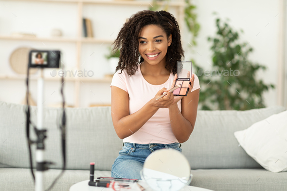 Beauty Blogger. African Woman Making Video Reviewing Cosmetic Products Sitting At Home. Selective Focus