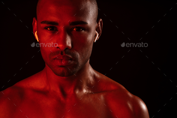 Image of african fitness man posing isolated over black wall background while listening music with earphones