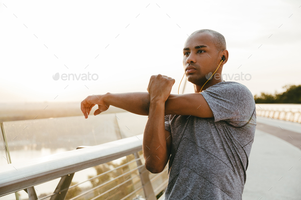 Relaxed african sportsman stretching while standing on the bridge