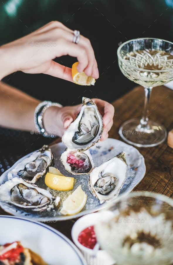 Woman squeezing lemon juice to oysters in plate with ice - Stock Photo - Images