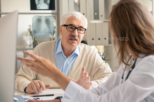 Senior patient in eyeglasses looking at doctor pointing at computer screen - Stock Photo - Images