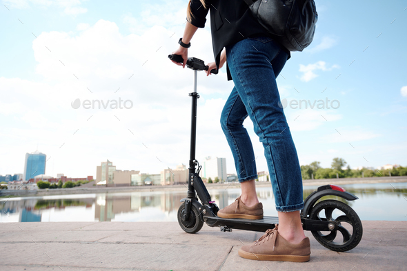 Contemporary young female on electric scooter standing in front of riverside - Stock Photo - Images