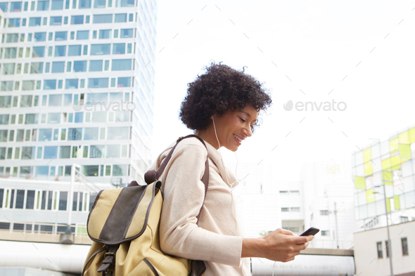 smiling woman walking in city with mobile phone and earphones - Stock Photo - Images