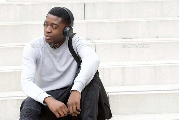 cool young african american man sitting on steps and listening to music with headphones - Stock Photo - Images