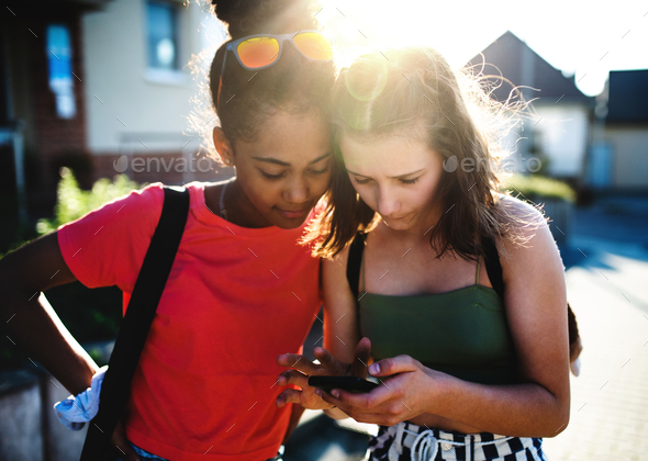 Teenager girls friends outdoors in city, using sartphone - Stock Photo - Images