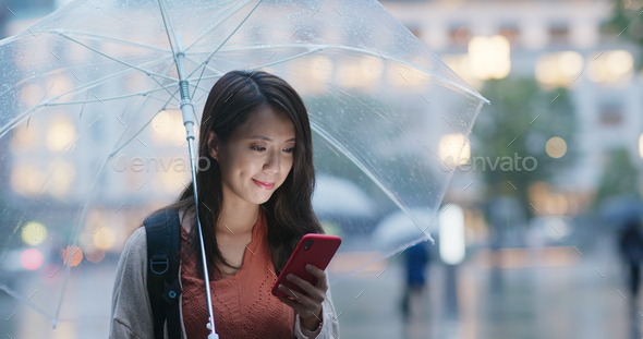 Woman hold with umbrella and use of mobile phone in the city at night - Stock Photo - Images