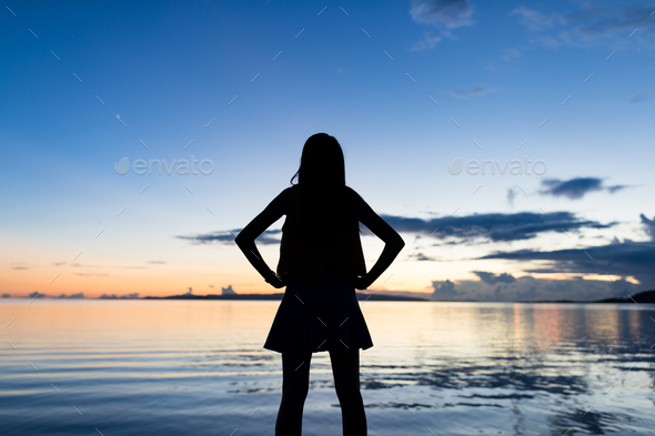 Silhouette of woman standing in front of the sea under sunset time - Stock Photo - Images
