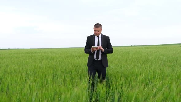 Business farmer standing on a young wheat field holding a tablet and studying the harvest. alt