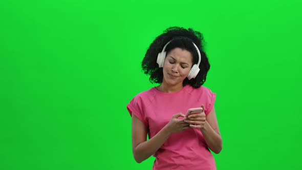 Portrait of Young Female African American Dancing and Enjoying Music in Big White Headphones Using alt
