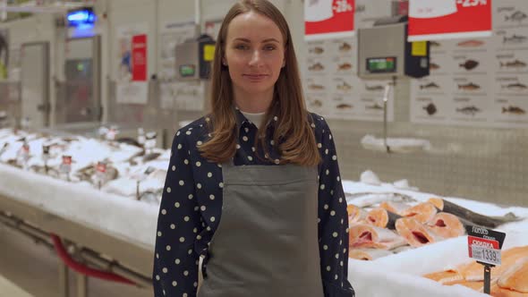 Young Saleswoman in an Apron Fish Shop Stands in Front of a Counter with Fresh Fish alt