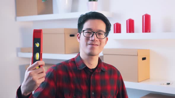 Young Asian Handyman Showing Thumb Up and Holding Leveller in the Other Hand alt