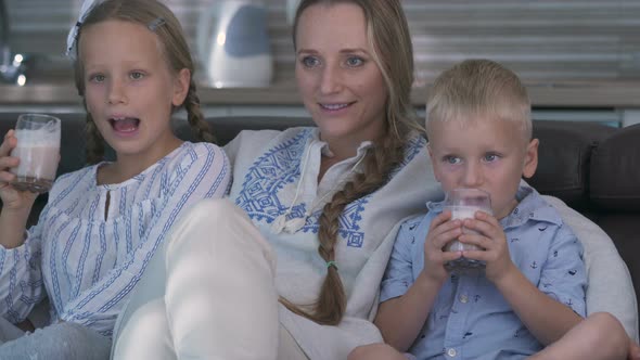 Mom and Two Children Watch TV While Sitting on the Couch, Children Drink Cocoa