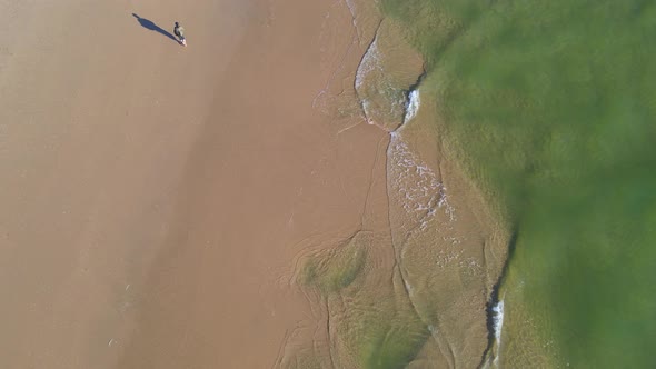 Aerial View of Person Walking Alone Along Coastline