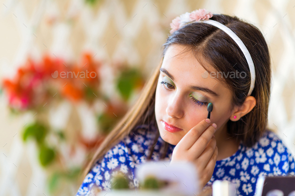 Young girl using her smartphone for an online beauty course learning about makeup carefully applying green eye shadow with an engrossed expression