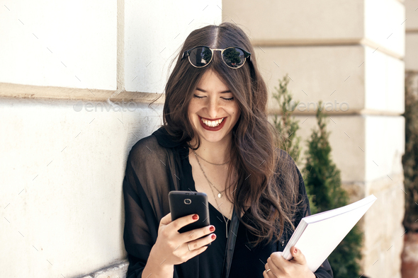 beautiful stylish woman using phone and holding magazine in city street - Stock Photo - Images