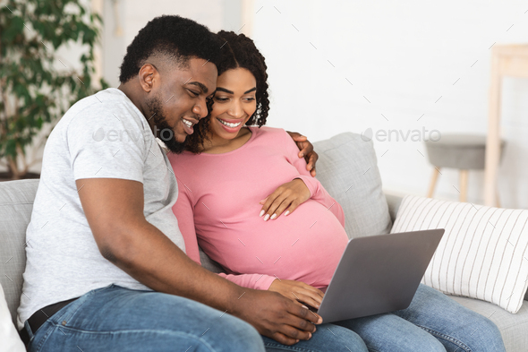 Happy african american expecting family using laptop at living room - Stock Photo - Images