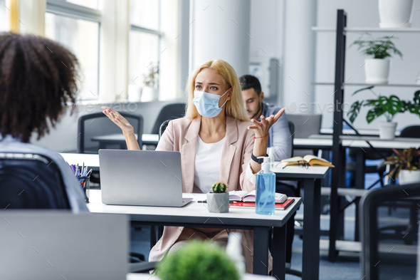 Conflict at work and problems with project. Angry woman in protective mask at workplace with laptop