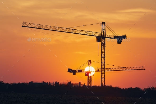 Building activity on contruction site. Silhouettes of cranes against sun.