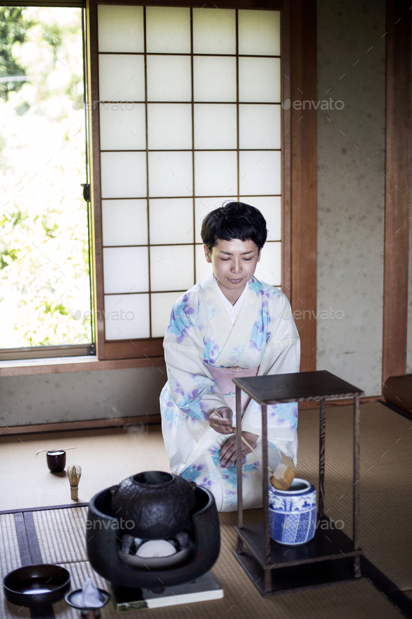 Japanese woman kneeling on tatami mat during tea ceremony. Stock Photo by Mint_Images