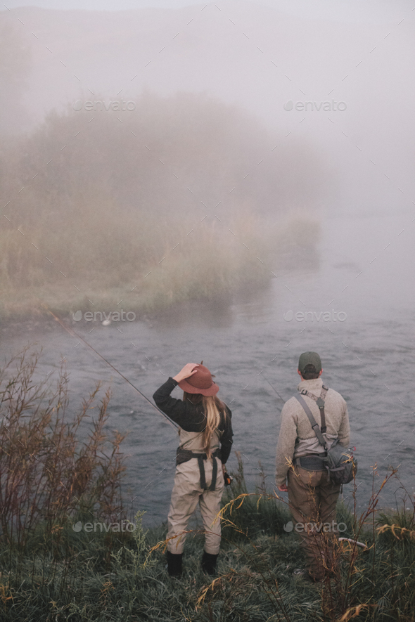 Two people, man and woman standing on the riverbank looking across the water. - Stock Photo - Images