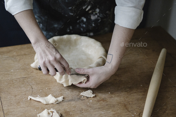 A woman using raw pastry dough to line a pie dish and finish the edge.