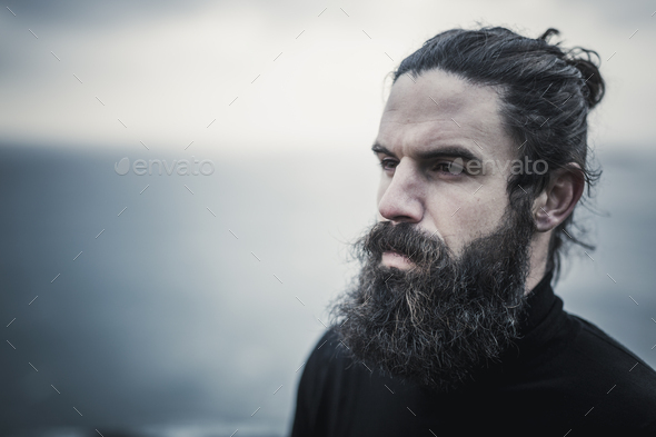 A man with full  beard and moustache and black hair scrapped back from his face. - Stock Photo - Images