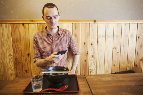 A western man in a noodle restaurant, using his smart phone. - Stock Photo - Images