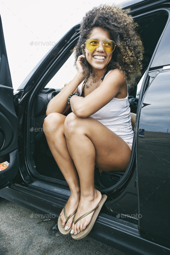 Portrait of smiling young woman wearing sunglasses, white vest and flip flops. - Stock Photo - Images